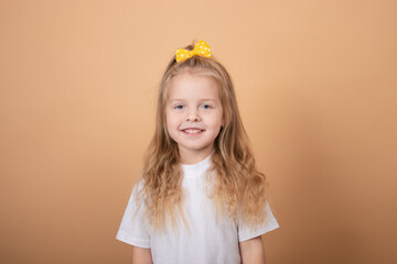 portrait of a sweet blonde little girl in white t-shirt and with yellow bow on her head. on brown background.