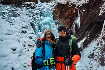 Smiling beautiful couple dressed in warm winter sportswear, sunglasses and gloves holding trekking...