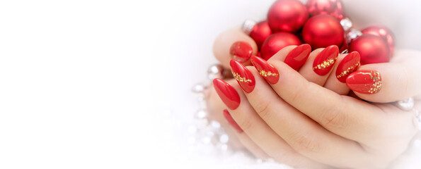 Red Christmas manicure with gold glitter. Beautiful female hands hold Christmas balls and beads. Photo of nails. Horizontal banner with place for text.