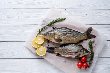 Fresh raw whole fish of mirror carp with spices, lemon and herbs on a background of parchment paper, lying on a wooden white background of boards