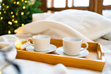 A wooden tray for eating in bed with two white tea cups. 