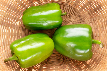 Three sweet green peppers in a straw bowl, close-up, top view.