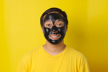 Man with cosmetics mask on the face on yellow background. Photo of man with perfect skin. Beauty and Skin care concept