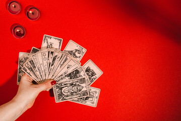 Esoteric magic composition top view with female hands of fortune teller reading Tarot cards on red...
