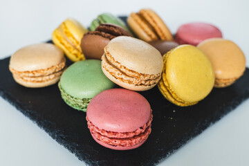 Colorful macaroons on a black slate stone served on a white table, Delicious French almond cookies, dessert.