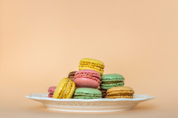 French macaroons on an apricot background. Delicious colorful almond cookies on a vintage plate, dessert. Place for text