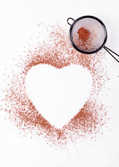 Cocoa powder framing heart shape copy space and strainer on the white table. Mockup with copy space