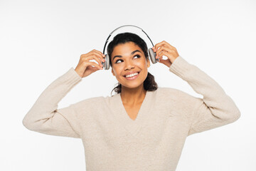 Cheerful african american woman in sweater holding headphones isolated on white.