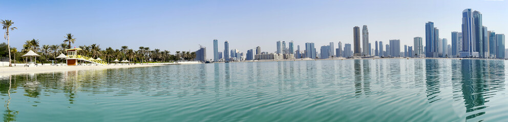 Fototapeta na wymiar Panorama beautiful Al Mamzar beach with white sand and palms on ashore of the Arabian Gulf on background modern skyscrapers of Dubai