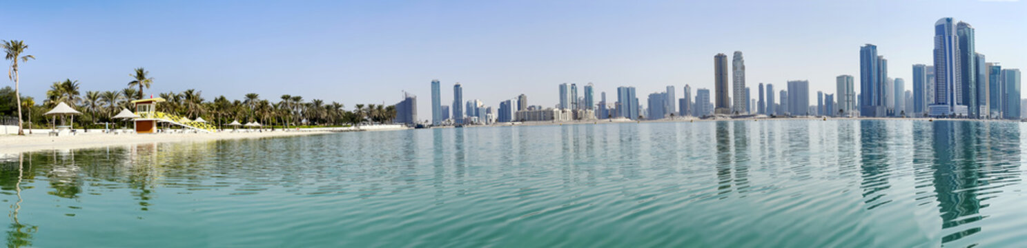 Panorama beautiful Al Mamzar beach with white sand and palms on ashore of the Arabian Gulf on background modern skyscrapers of Dubai