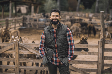 Fototapeta na wymiar A farmer in the black vest and a plaid shirt standing near the cattle-pen