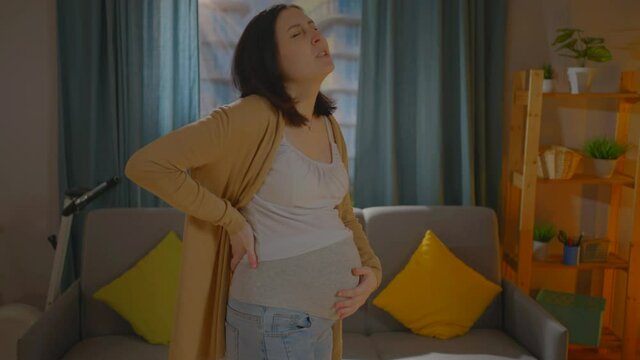 young pregnant woman feels pain discomfort in the lower back against the background of a home environment