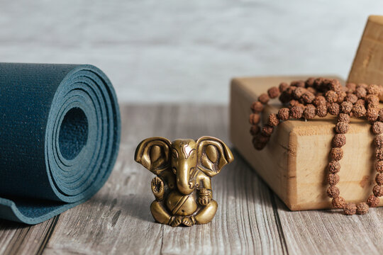 Close-up bronze statue of hindu god of success Ganesha. Japa Meditation accessories, mat and yoga wooden blocks on wooden background.