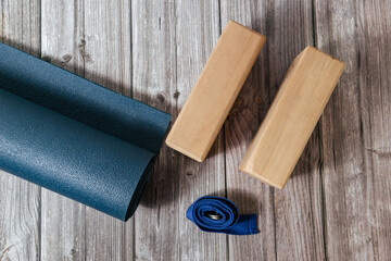 Closeup of two wooden yoga blocks, belt and blue yoga mat on the wooden floor. Fitness, stretching...