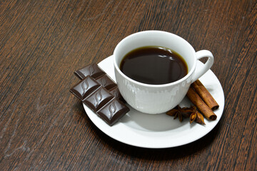 cup of coffee with chocolate, cinnamon rolls and badian on dark wooden kitchen table