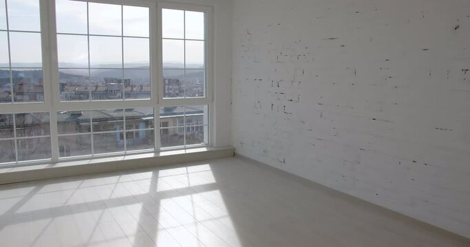 A door is opening and the camera enters an empty unfurnished room interior with a wooden parquet floor, white walls, and big windows. 4k slow motion
