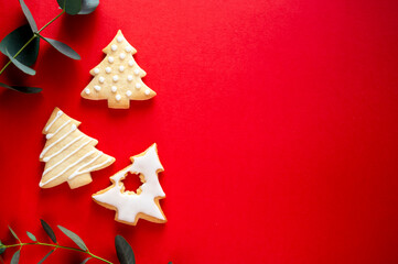Christmas tree shaped cookies with eucalyptus leaves on red background with copy space