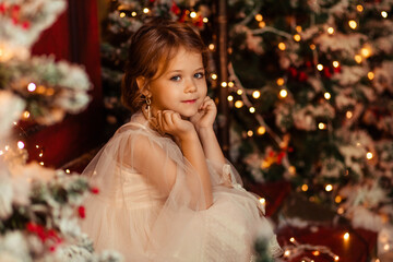 portrait of a beautiful girl with long hair in an elegant dress at home by the Christmas tree