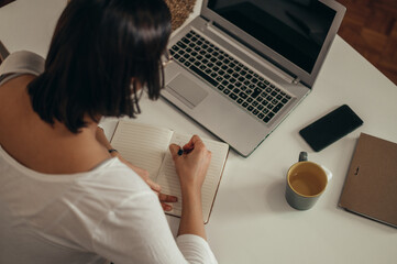 Woman writing in a notebook and using a laptop while working from home