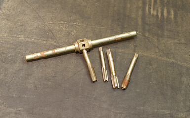 A set of used taps and tap wrench for internal threading.