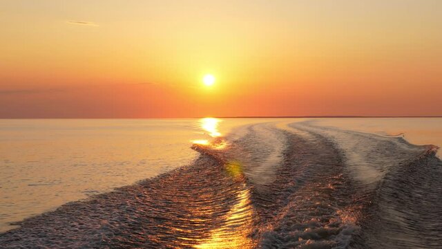 Beautiful vivid sunset at calm lake or sea, camera look back from fast running motorboat. Wave from vessel and sun light reflection on water. Get away from it all concept