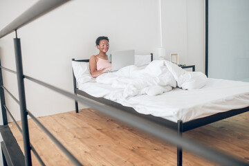 A young woman with a laptop in bed at home