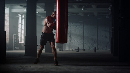 Man with muscular body punching bag in gym. Afro guy kicking sports bag