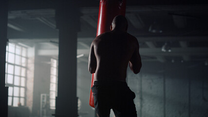 Boxer punching sports bag. Strong man working out blows on punching bag