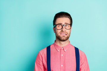 Fototapeta premium Photo of doubtful unhappy upset young man look empty space wear glasses bite teeth isolated on teal color background