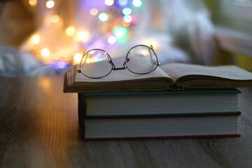 Open book and reading glasses with candles and colorful bokeh lights in the background. Selective focus.