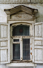 A window with wooden shutters and carved frames of the old house, with stucco elements on the facade. The picture was taken in Russia, in the city of Orenburg