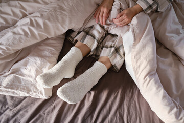 The girl lies in bed in pajamas and warm socks. Women's legs in cozy white fluffy socks in bed....