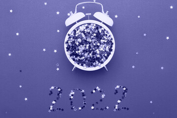 Fototapeta na wymiar Alarm clock and star shaped confetti on blue background. Very Peri color of the year.