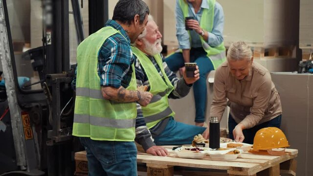 Smiling Storage workers sits and have a break. Colleagues eat a sandwich and drink coffee during the break for lunch