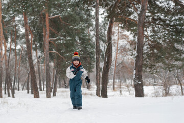 Fototapeta na wymiar Little boy runs merrily through snow. Child plays in winter forest on large fir trees background.