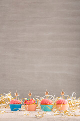 Golden candles in the shape of star on cupcakes. Muffins with pink buttercream frosting on festive tinsel background. Copy spacve on gray background. Vertical frame