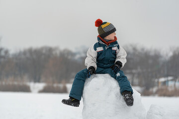 Child playing in snow castle. Portrait of boy on large block of snow in winter park.