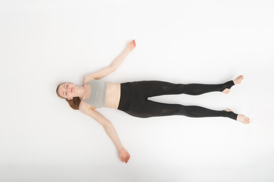 Shavasana. Corpse Pose. Yoga asanas. Young slender woman in sportswear lies on the white floor . Top view.