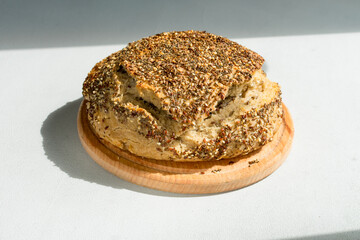 Natural loaf of yeast-free sourdough bread with sesame seeds, flax, chia, sunflower seeds, on a wooden board on the table, close-up.