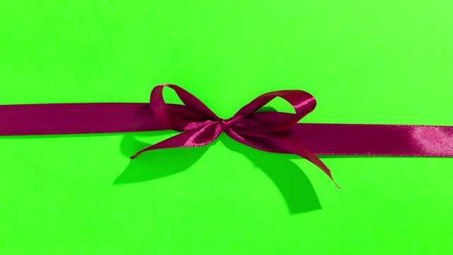 Red ribbon with bow on green screen, opening and unpacking a gift, top view - Stop motion animation for Valentine's Day, Christmas.