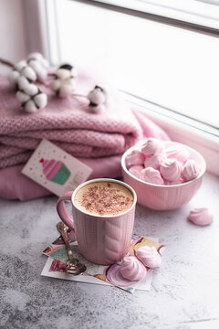 Photos in trendy pink tones. Still life on the window: cappuccino coffee with marshmallows on a light gray background. Home comfort. Selective focus.