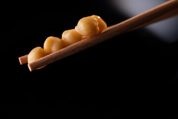 garbanzos cocidos cogidos con dos palillos. Plato negro en el fondo