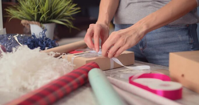 Woman wrapping holyday gift, decorating stylish gift in craft paper on table in home