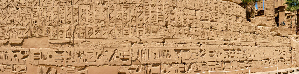 Fototapeta na wymiar Panoramic view of the wall with Egyptian hieroglyphs and ancient drawings at Karnak Temple. Luxor, Egypt.