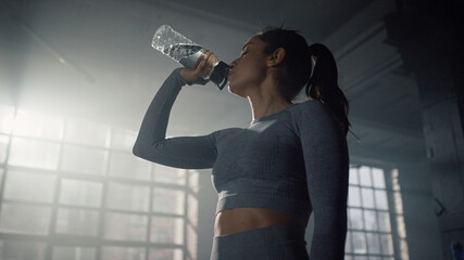 Sportswoman drinking water in gym. Girl taking rest after fitness workout 