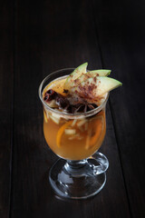 Mulled wine based on white wine. A cocktail of white wine, fruits and spices. Drink in glass goblet on a black background. A hot drink for health. Vertical photo.