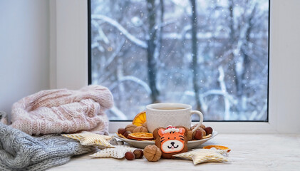 Coffee cup, biscuit cookies with tiger, dried orange slices, nuts, decor on window sill.  snowy...