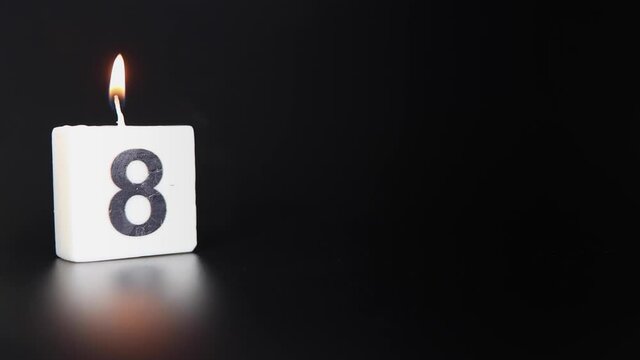 A square candle saying the number 8 being lit and blown out on a dark black background celebrating a birthday or anniversary