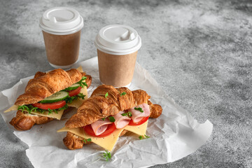 Croissant sandwich with a cup of coffee, gray grunge background. Croissants with ham and fresh...