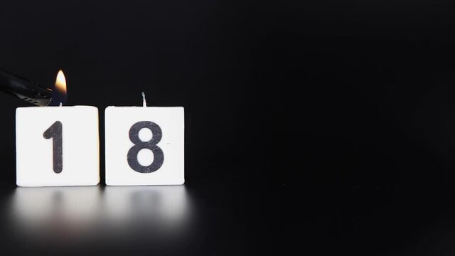 A square candle saying the number 18 being lit and blown out on a dark black background celebrating a birthday or anniversary